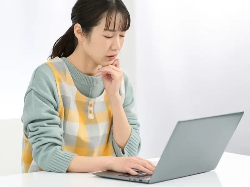 パソコン作業で悩むエプロンを着た女性の画像