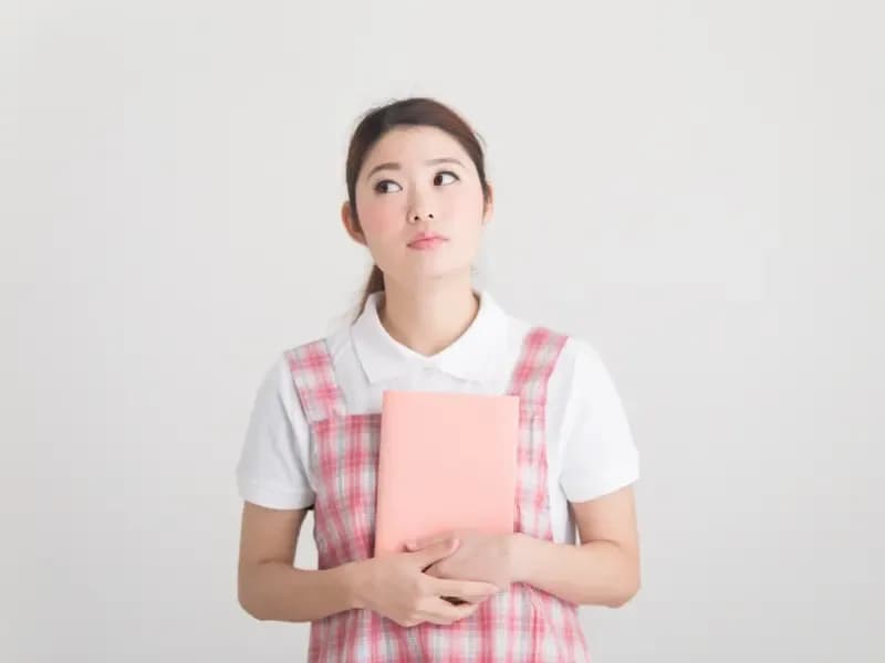 ノートを持って考え事をしている保育士の画像