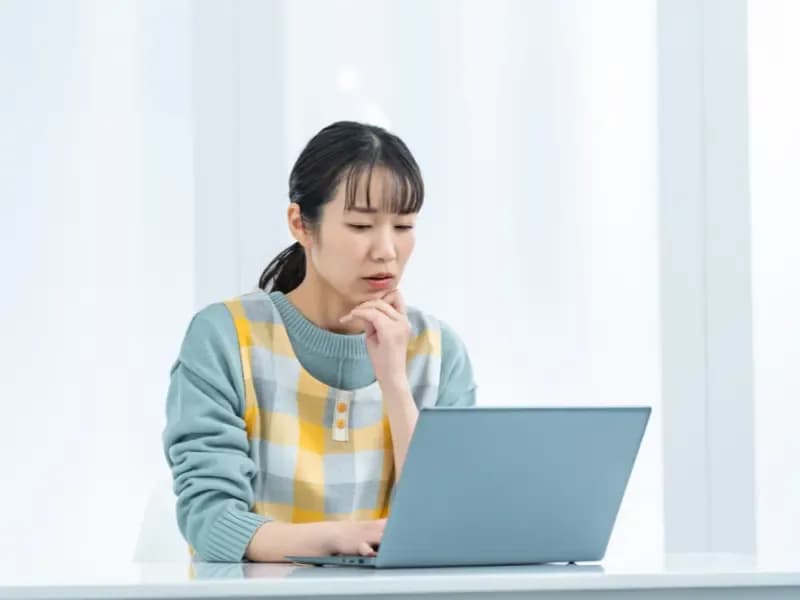 パソコンを見ながら悩む保育士の画像