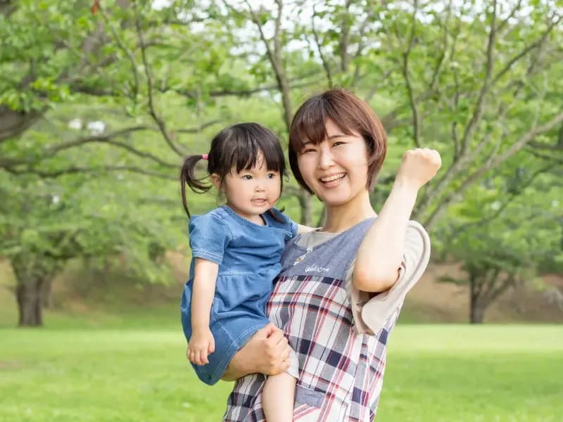 子どもを抱っこしてガッツポーズをする保育士の画像