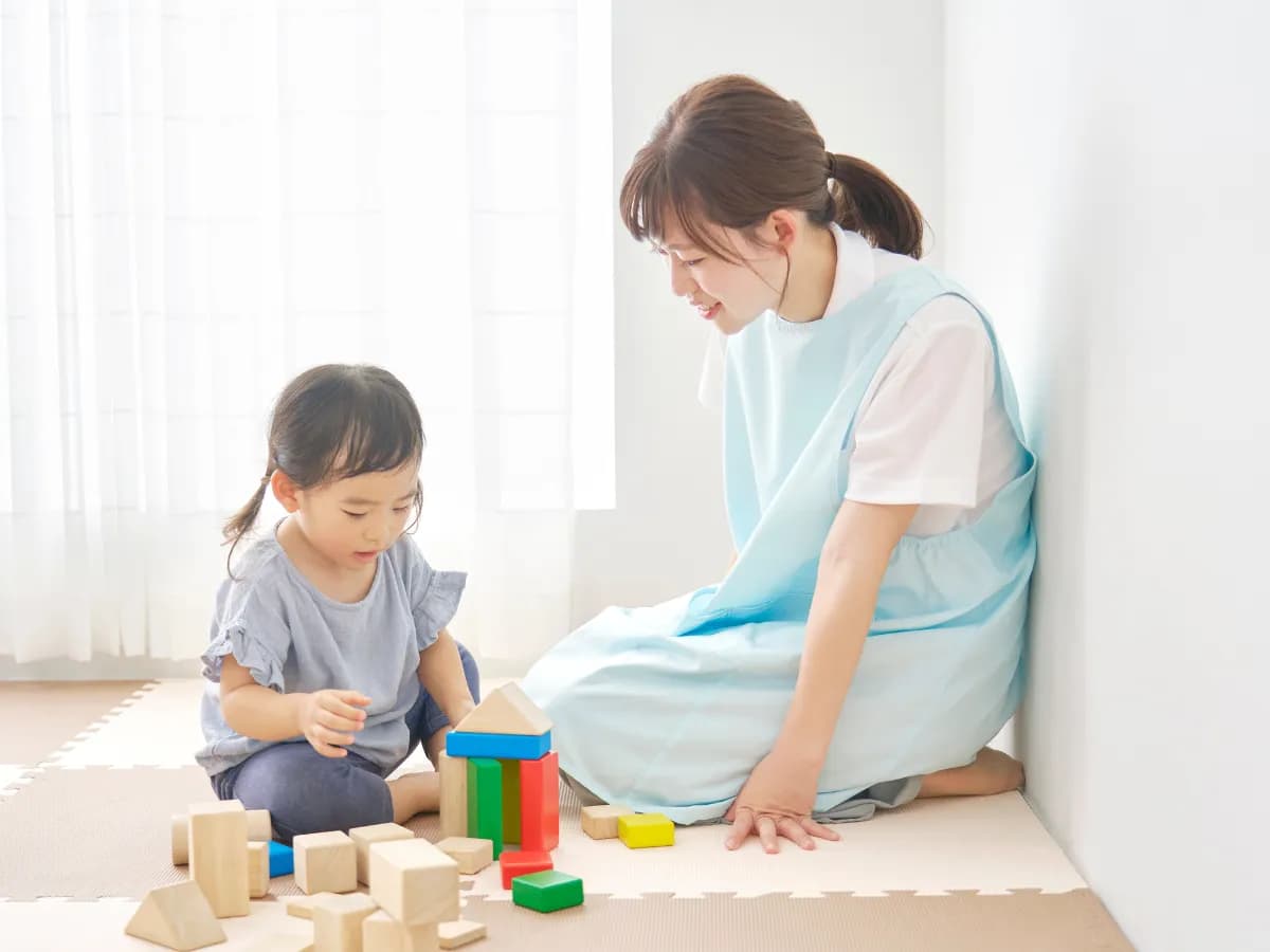 積木で遊ぶ保育園児と若い女性の保育士の画像