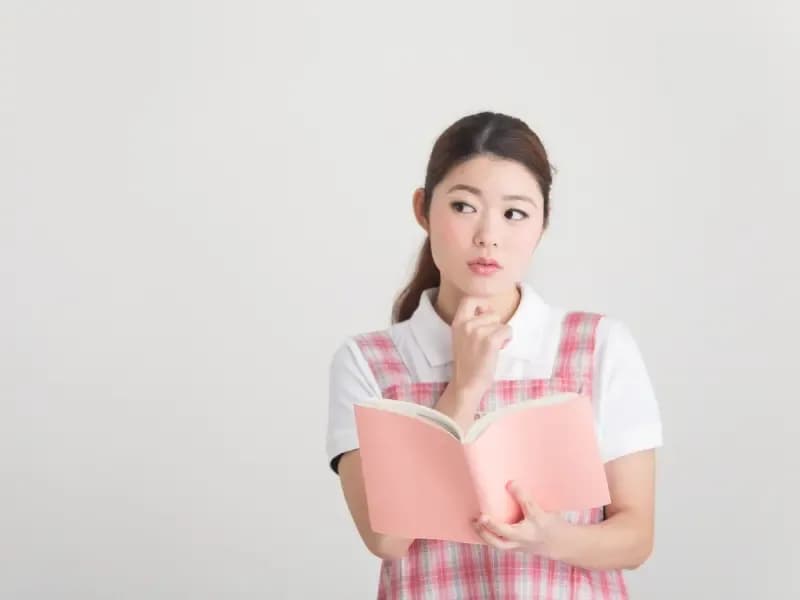 本をもって悩む保育士の画像