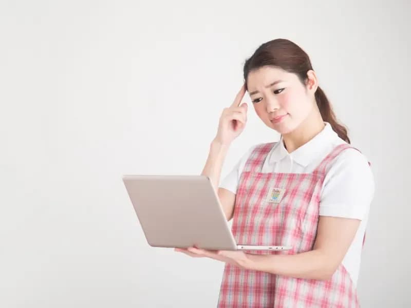パソコンを持って考える保育士の画像