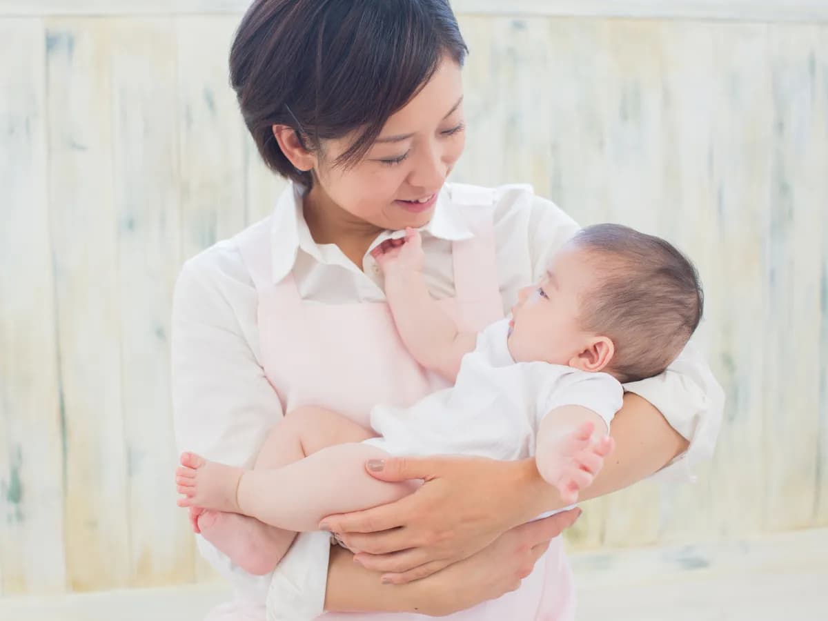 赤ちゃんを抱っこするエプロン姿の女性の画像