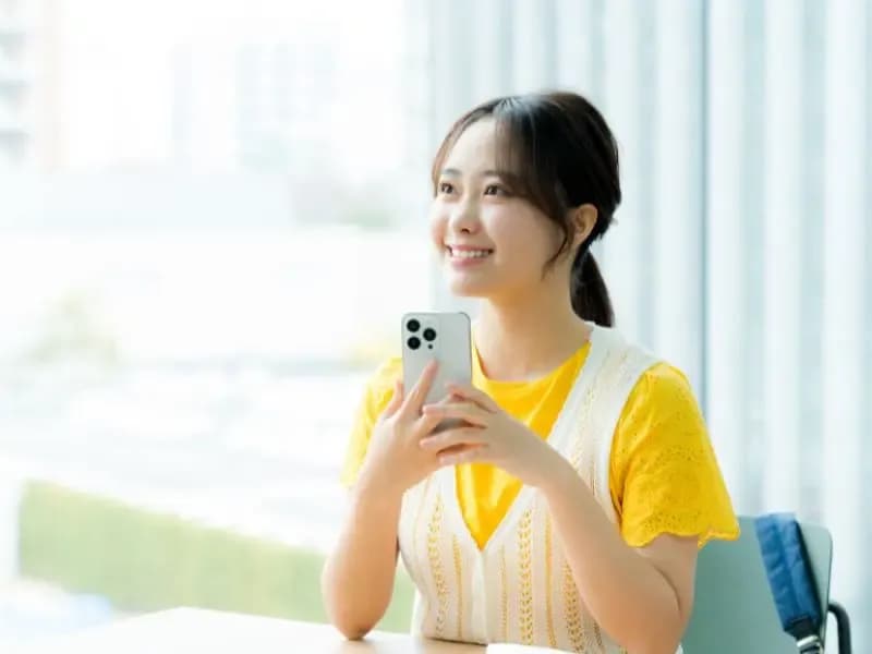 スマホを持ち考え事をする女性のイメージ