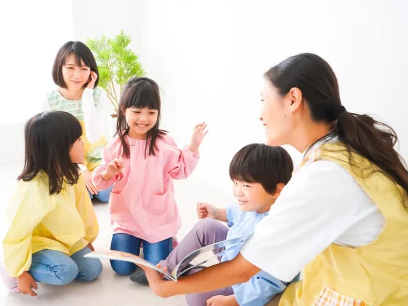 複数の園児を相手に読み聞かせをする保育士の画像