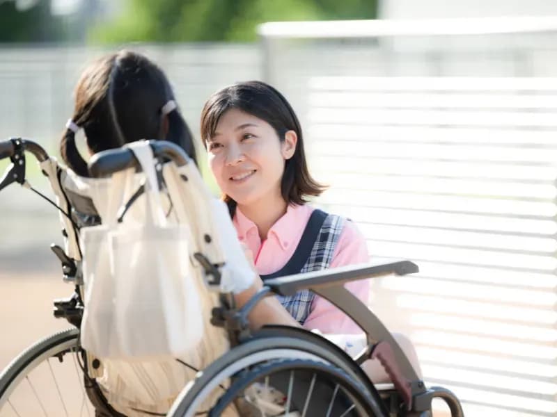 車いすに乗る女児と会話をする保育士の画像