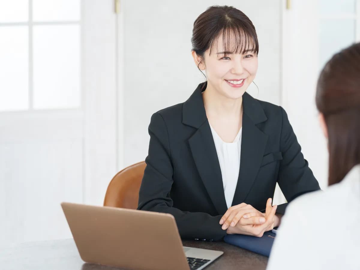 ノートパソコンを前にスーツを着た女性が女性と笑顔で対話している様子