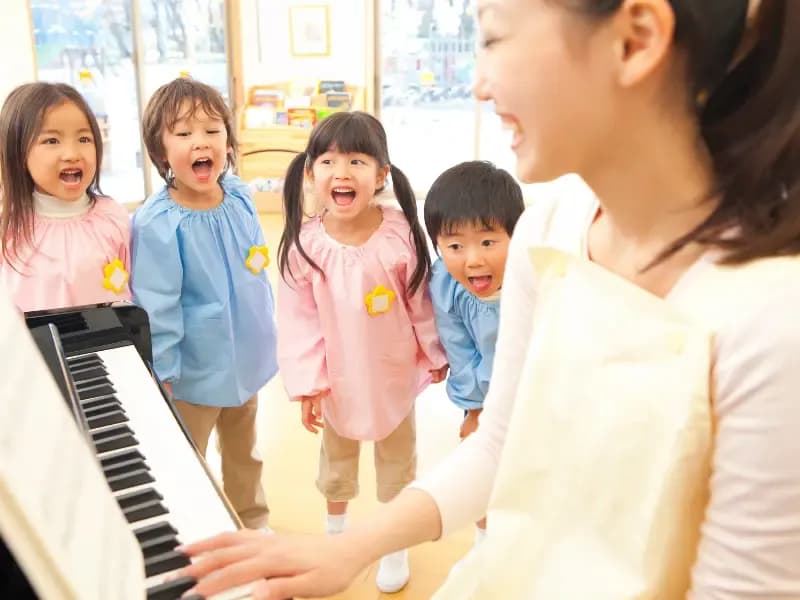 幼稚園教諭のピアノに合わせて歌う幼稚園児のイメージ