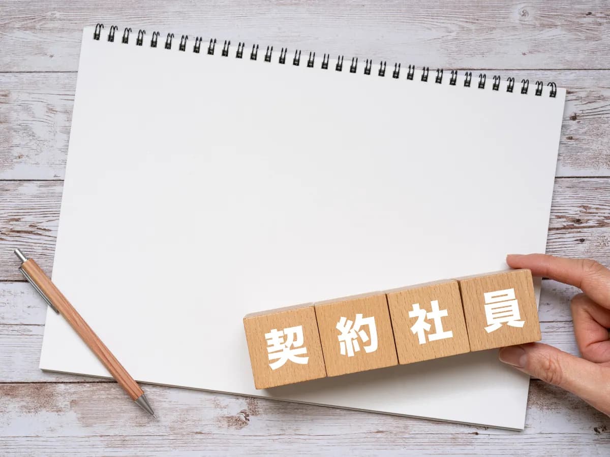 契約社員と書かれたブロック、ノート、ペン、手の画像