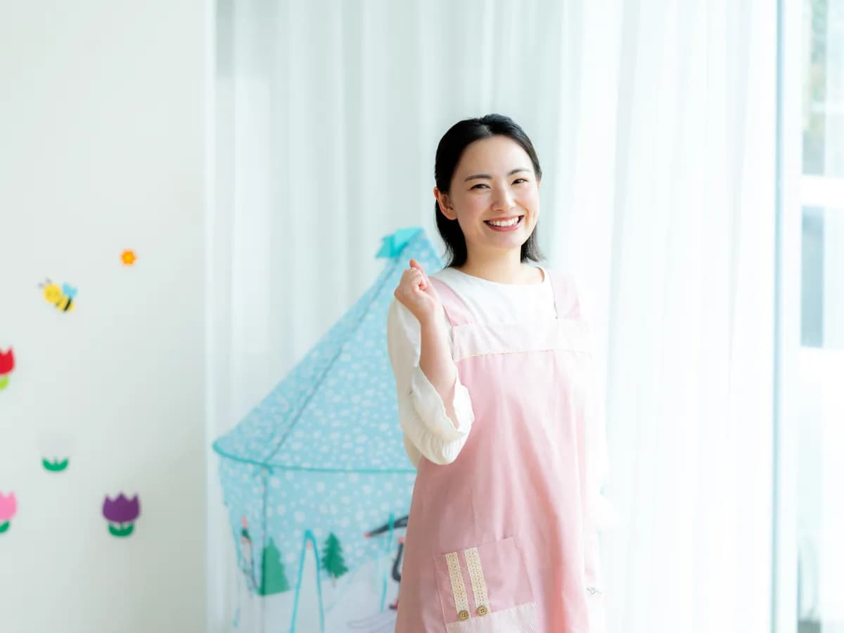 子供用テントの前で笑顔でガッツポーズをする保育士のイメージ