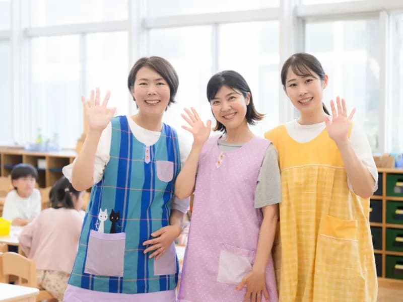 片手を挙げる3人の保育士の画像
