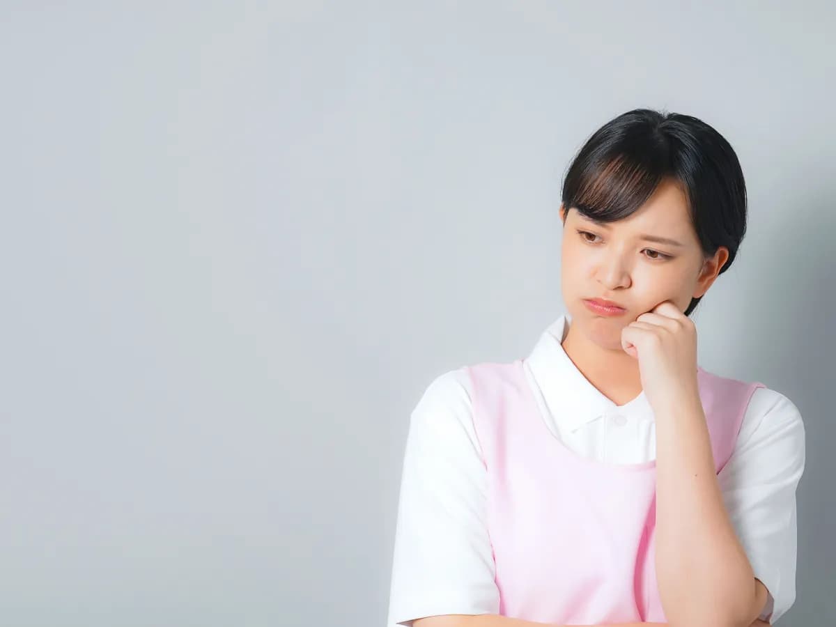 頬に手を当てて悩む若い保育士のイメージ