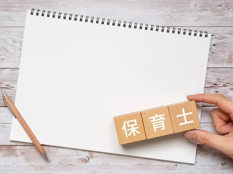 紙の上に保育士と書かれた積木を持つ手のイメージ
