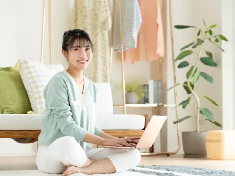 ノートパソコンを膝の上に載せて笑顔の女性のイメージ