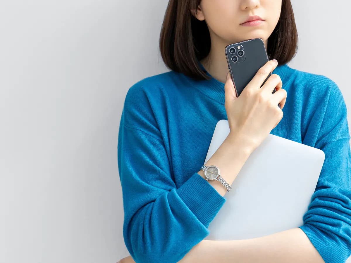 スマホを片手に考える女性の画像