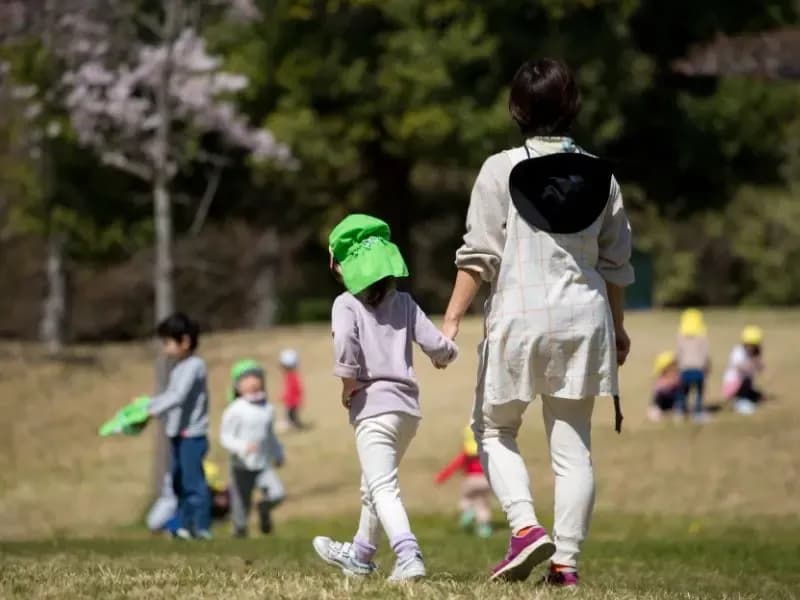 原っぱで遊ぶ子供と先生のイメージ