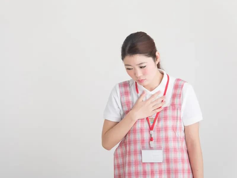 胸に手を当ててうつむく保育士の画像