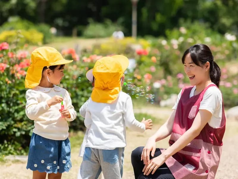 シャボン玉を吹く園児と笑顔の保育士の画像