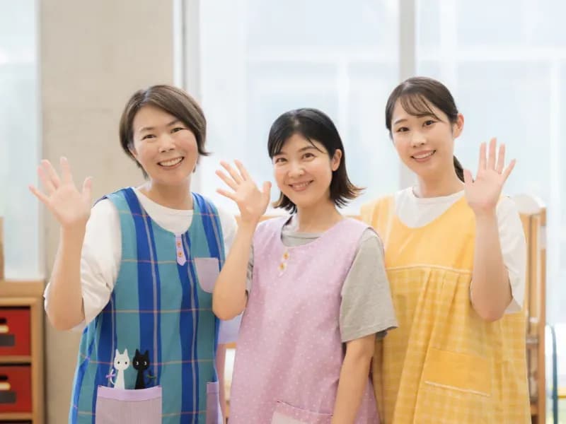 片手を挙げて微笑む保育士の画像