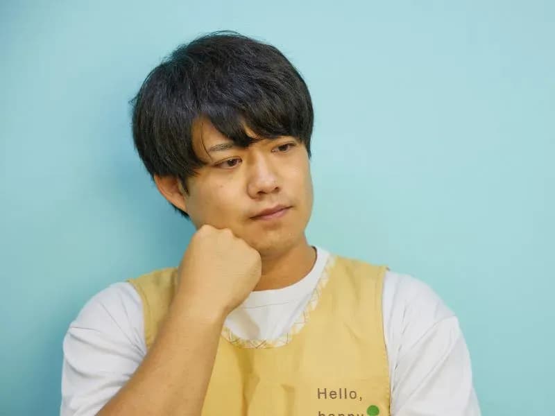 顎に手を当てて悩む男性保育士の画像
