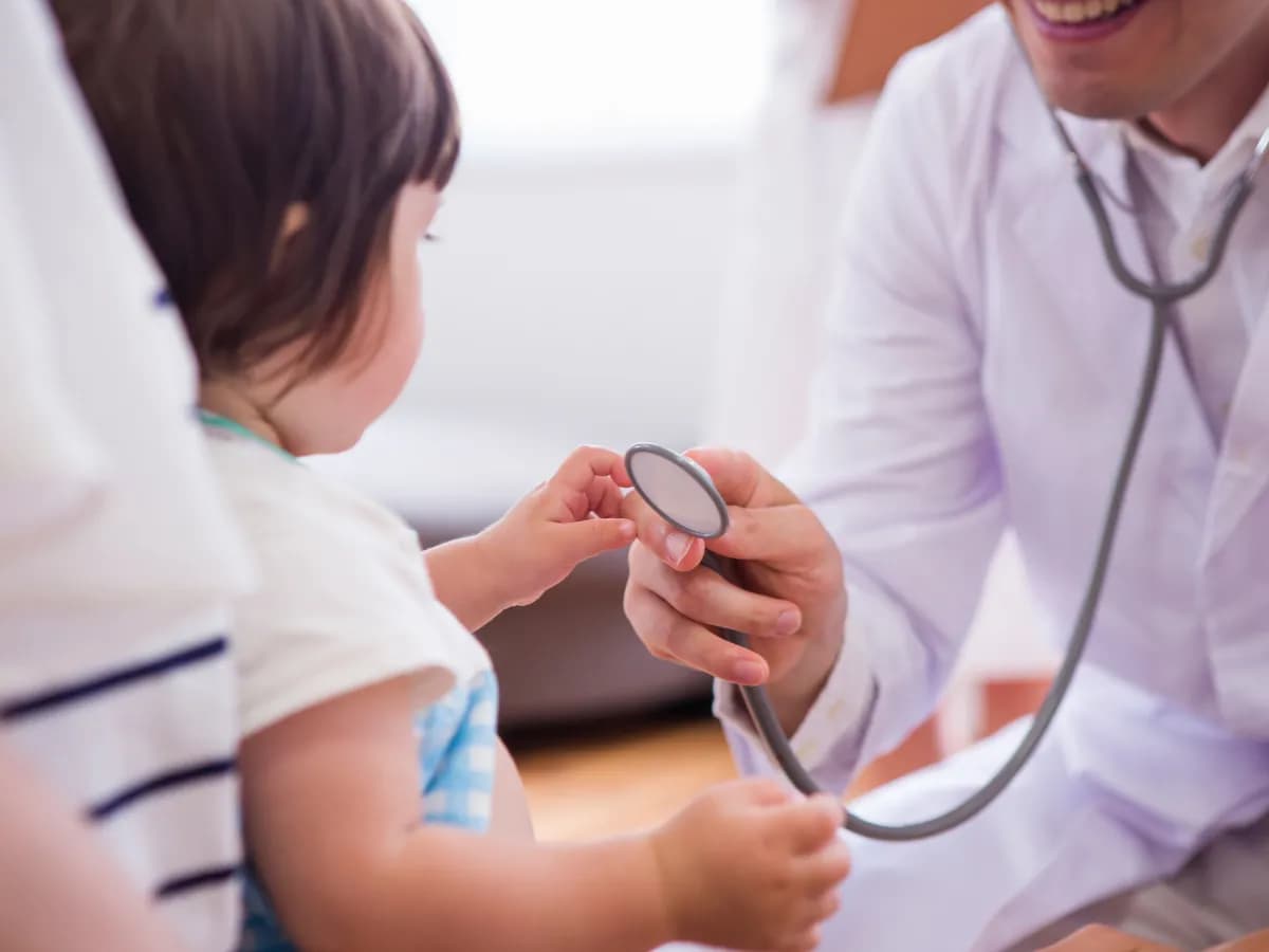 子供と保育士の後ろ姿と聴診器をあてる医師の画像