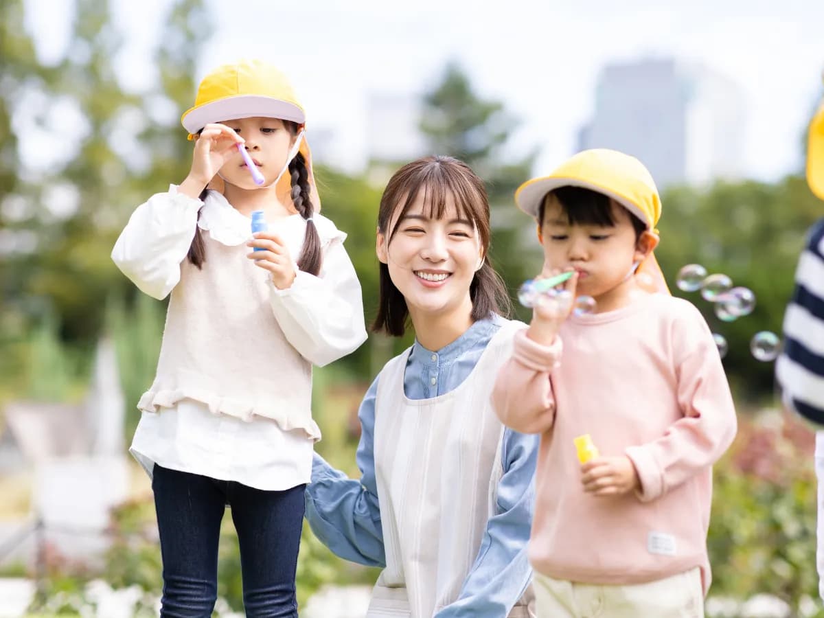 シャボン玉で遊ぶ園児と笑顔で見守る女性保育士のイメージ