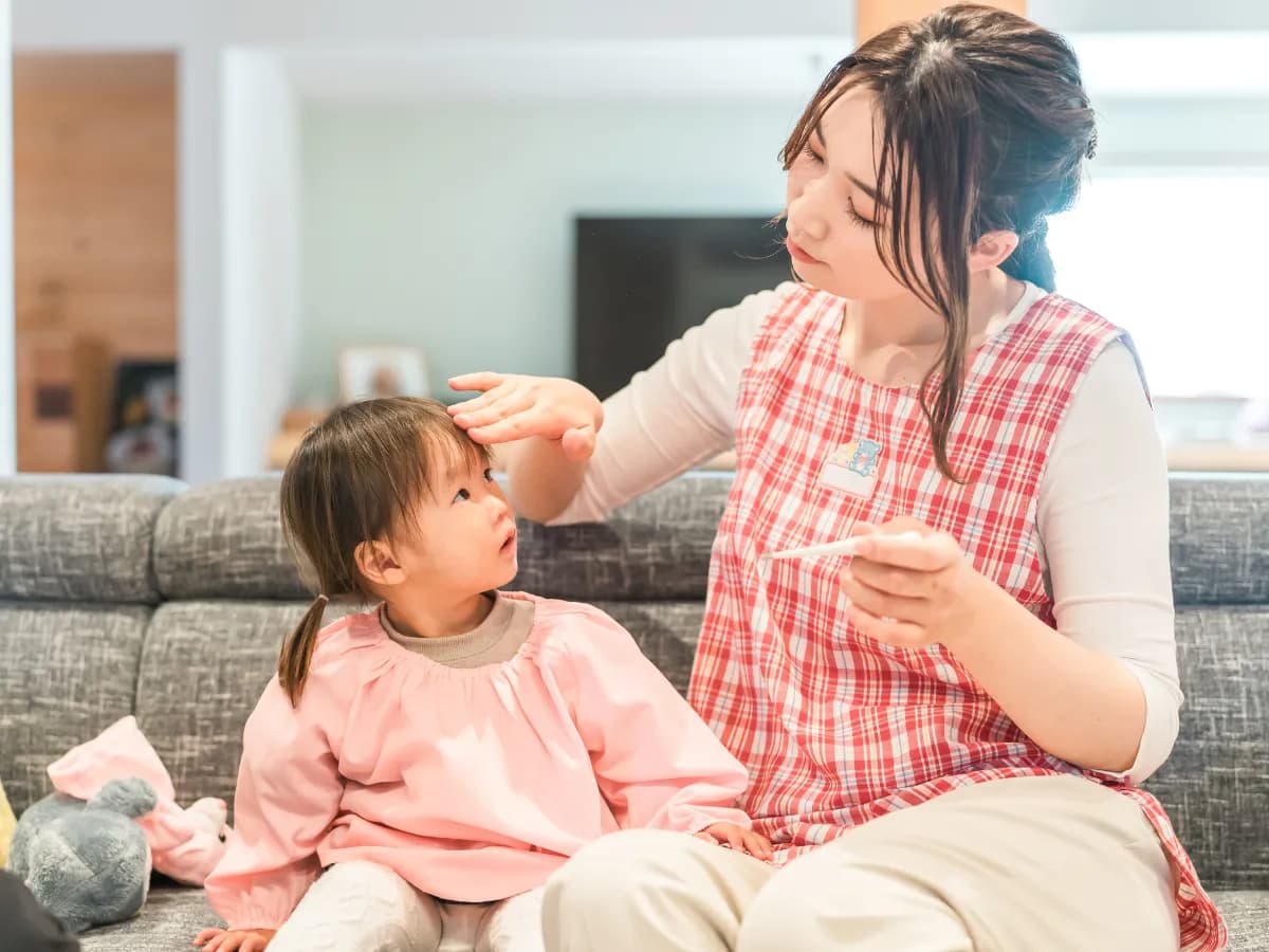 子供の体温を測る保育士のイメージ