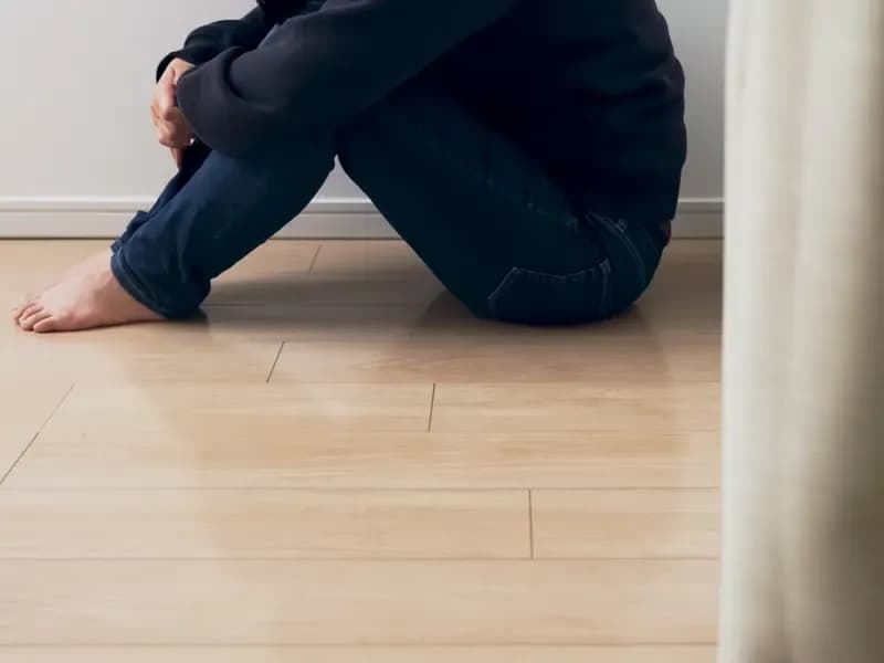 自宅で足を抱えて落ち込む保育士のイメージ