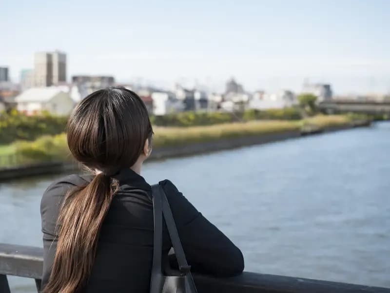 川を眺めて転職を考える若い女性の後ろ姿のイメージ