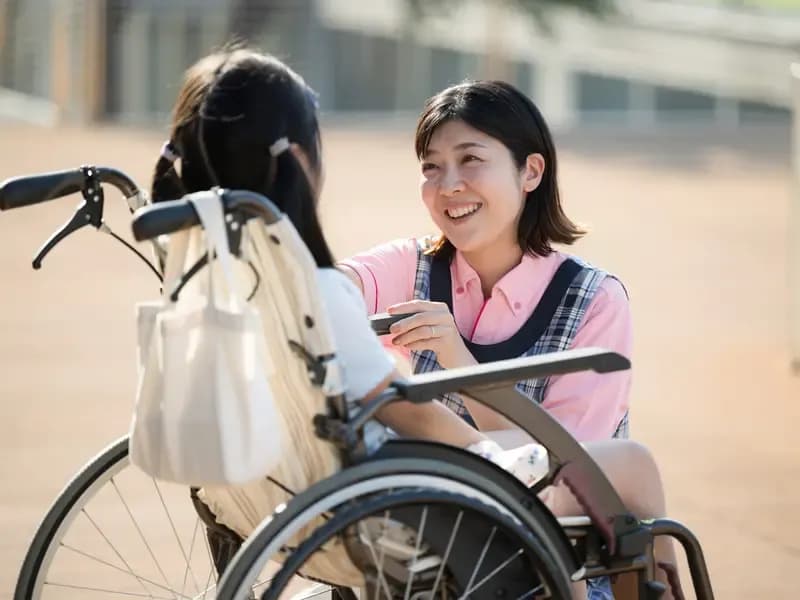 車いすの少女と笑顔で話す指導員のイメージ