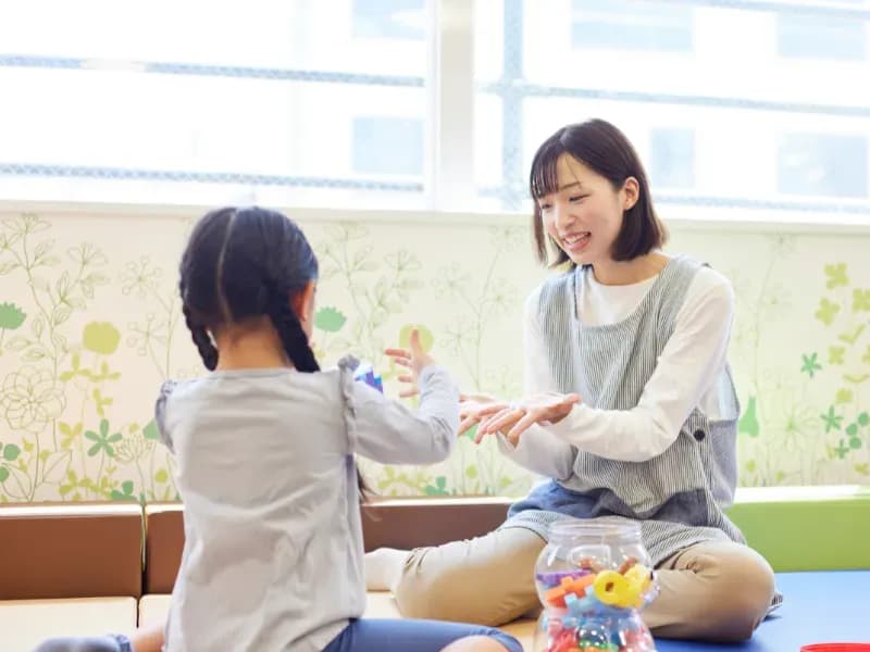 託児所でおもちゃで子供と遊ぶ保育士の画像