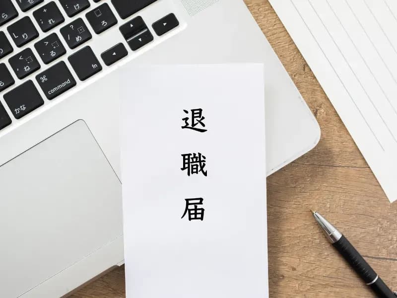 デスクの上にあるパソコンとペンと退職届の画像