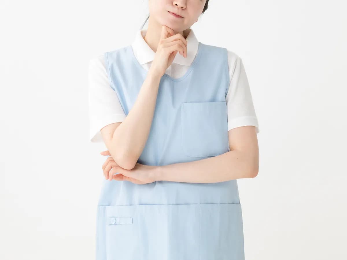 顎に手を当てて考える青いエプロン姿の女性の画像
