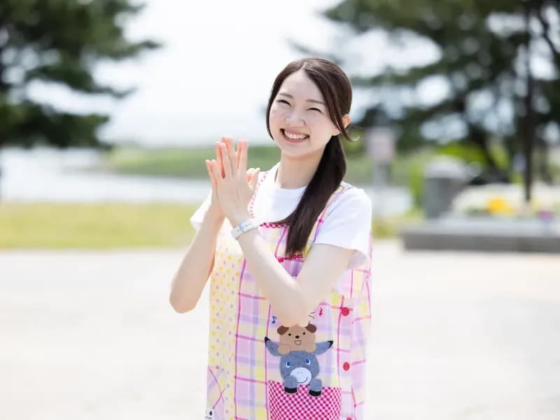 屋外で手を合わせて微笑む保育士の画像