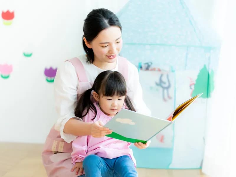 園児に絵本を読む保育士の画像