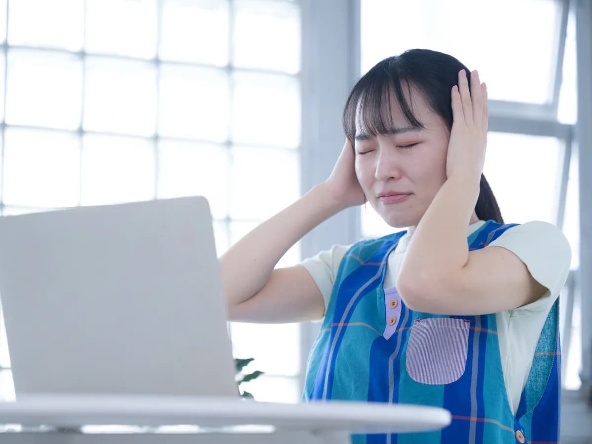 ノートパソコンの前で頭を抱え悩む保育士の女性のイメージ