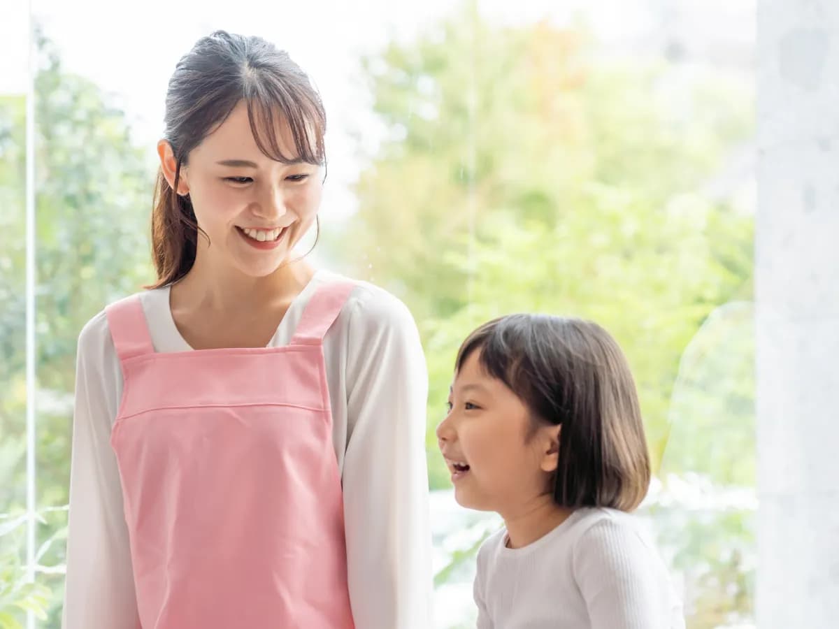 窓際で笑顔で会話する保育士と園児のイメージ