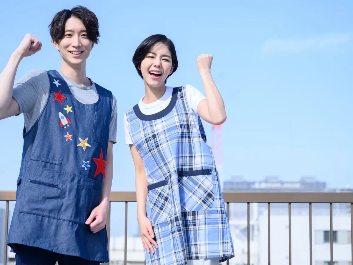 屋上で笑顔でガッツポーズをする若い男女の保育士の画像