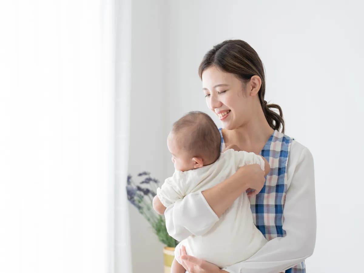笑顔で赤ちゃんを抱っこするベビーシッターの女性の画像