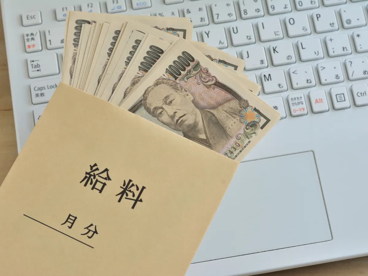 ノートパソコンと給料袋に入った複数の一万円札の画像