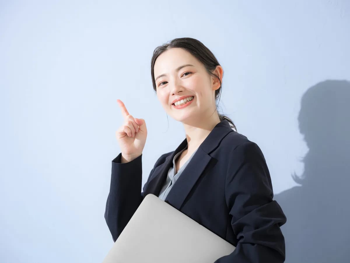 パソコン持ってスーツを着た立つポイントなどの指差しポーズの若い女性のビジネス上半身の画像
