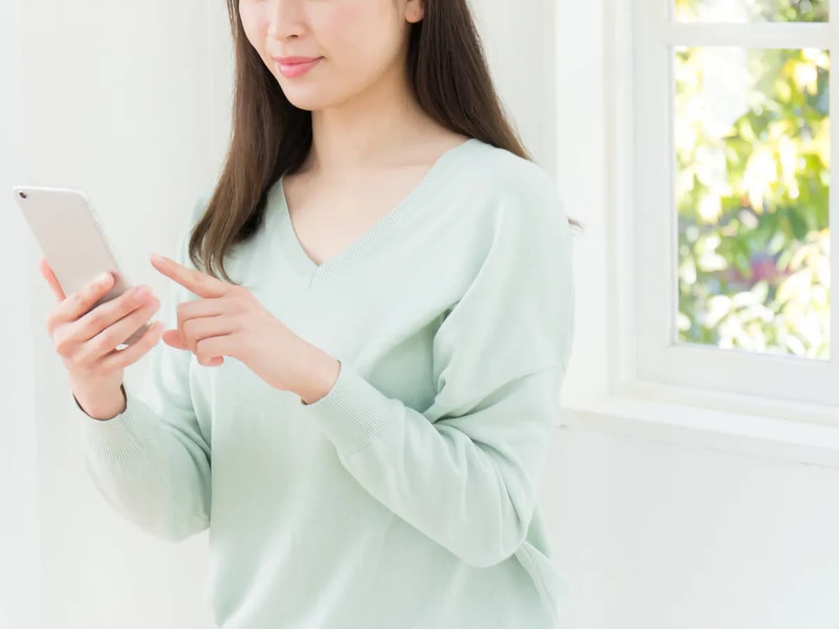 スマホを片手に操作する薄緑の服を着たロングヘアの女性の画像
