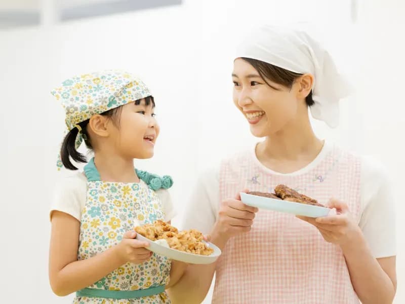 給食のお皿を持つ保育士と園児の画像