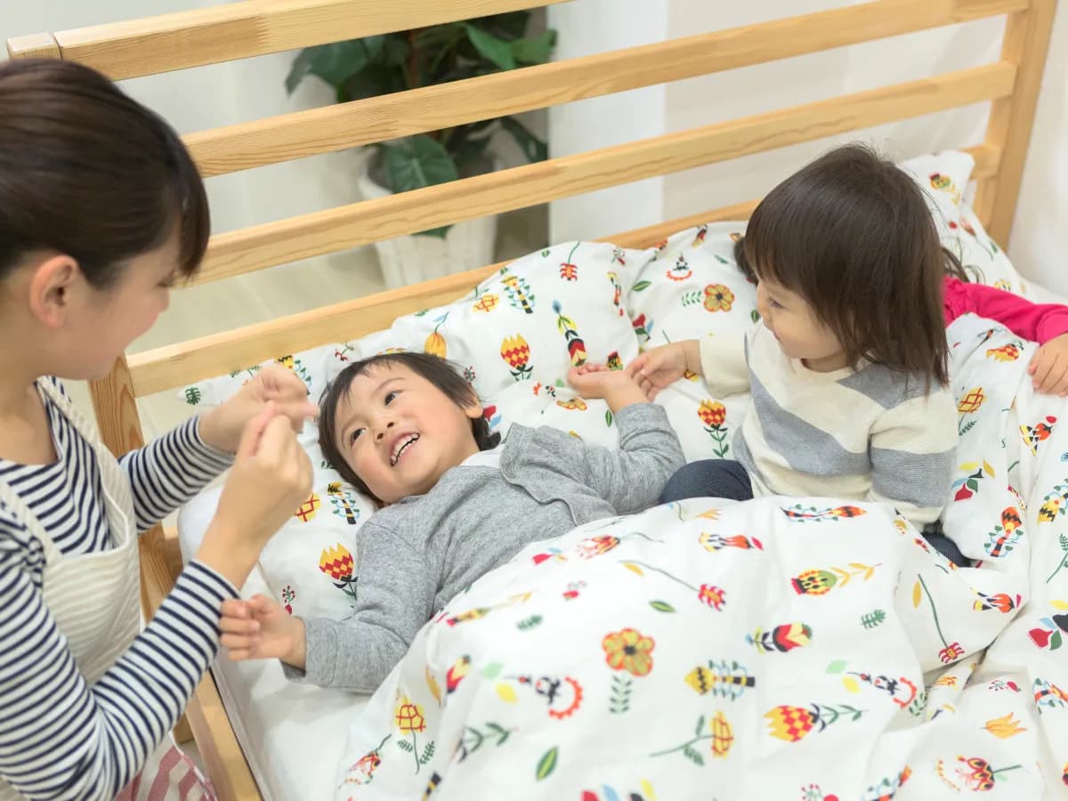 ベッドで子供たちを寝かしつける保育士の画像