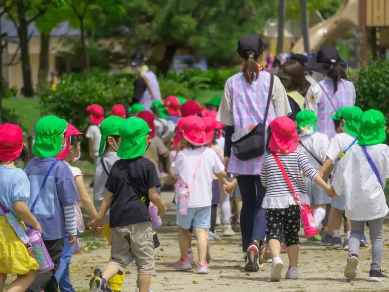 園帽を被った保育園児達と手をつなぎ歩く保育士のイメージ