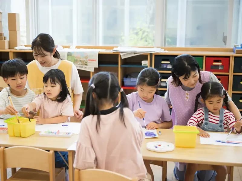 保育士と一緒に絵の具で製作をしている園児達の様子