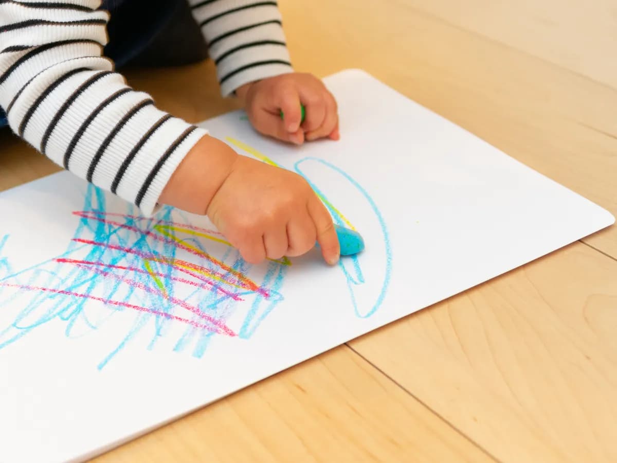床に紙を置いてお絵描きをする子供の手の画像