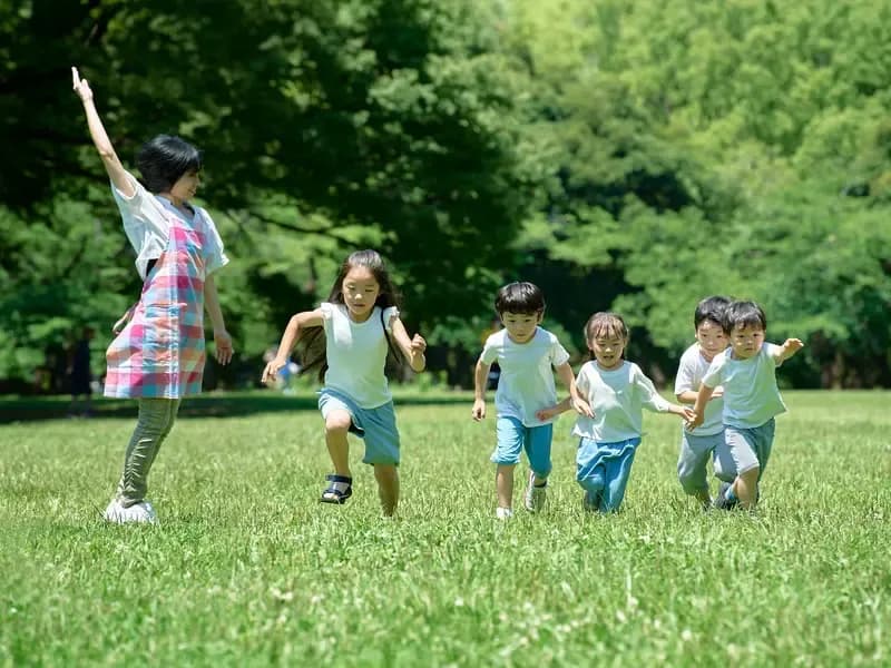芝生でよーいドンの合図をする保育士とかけっこをする保育園児のイメージ