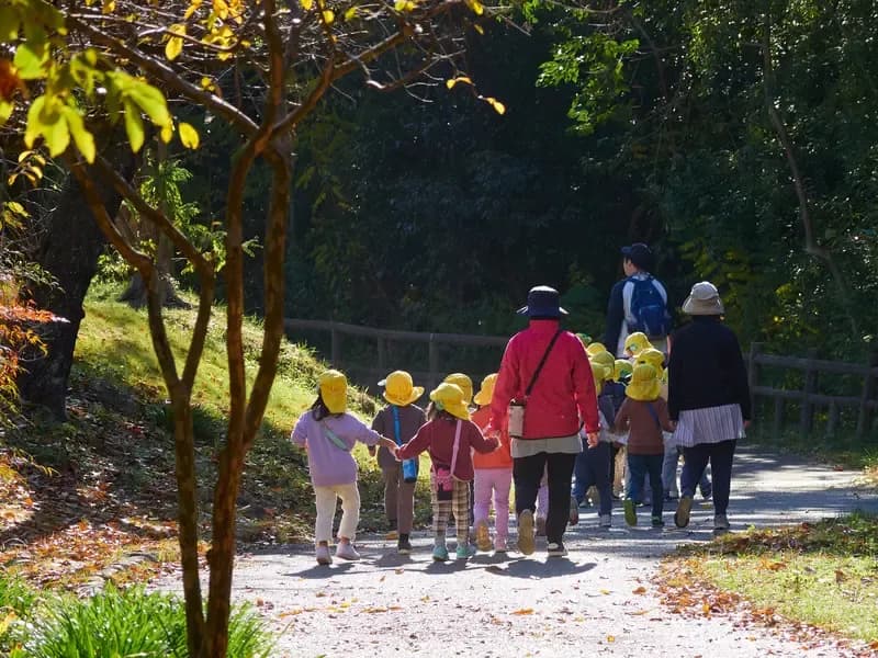秋の公園で散歩している保育園の園児と先生のイメージ